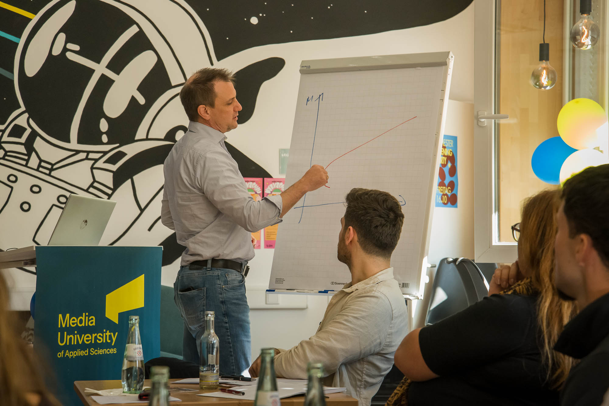 Ein Referent zeichnet an einem Flipchart und erklärt etwas an einer Kurve.